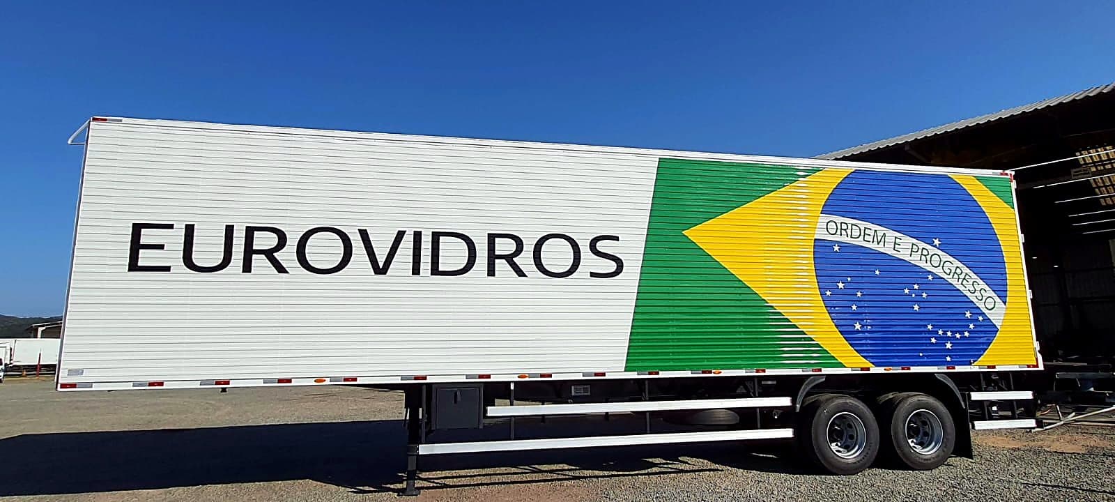 Semirreboque baú branco da Eurovidros com o nome da empresa e a bandeira do Brasil pintados na lateral
